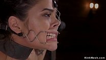 Brunette hottie in standing bondage position with wrists and neck in metal stock gets gagged by master